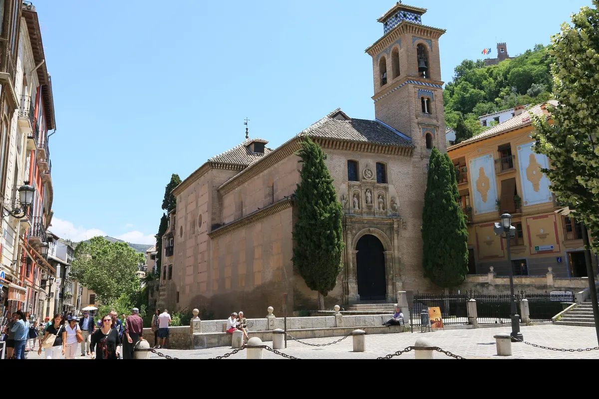 The brick bell tower and doorway of the church of Santa Ana beside Plaza Nueva, with a tower of the Alhambra on the wooded hill behind